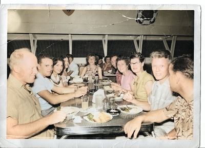 Restored and colorized (AI-assisted); faces are the original photo, colours are a best guess. Family group at a restaurant table, c. 1955–60.