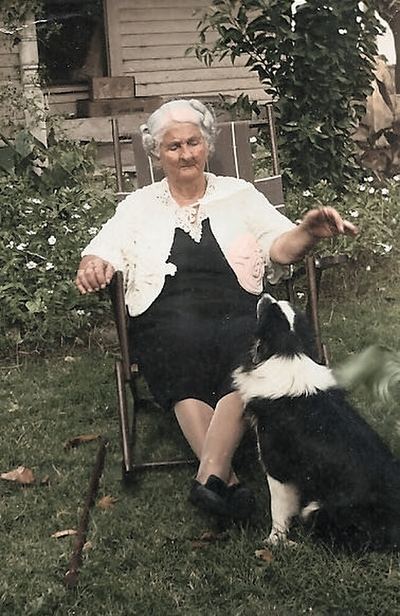 Restored and colorized (AI-assisted); faces are the original photo, colours are a best guess. Grandma Walker — Nancy Jane Higginbotham Walker, seated outdoors with a dog.